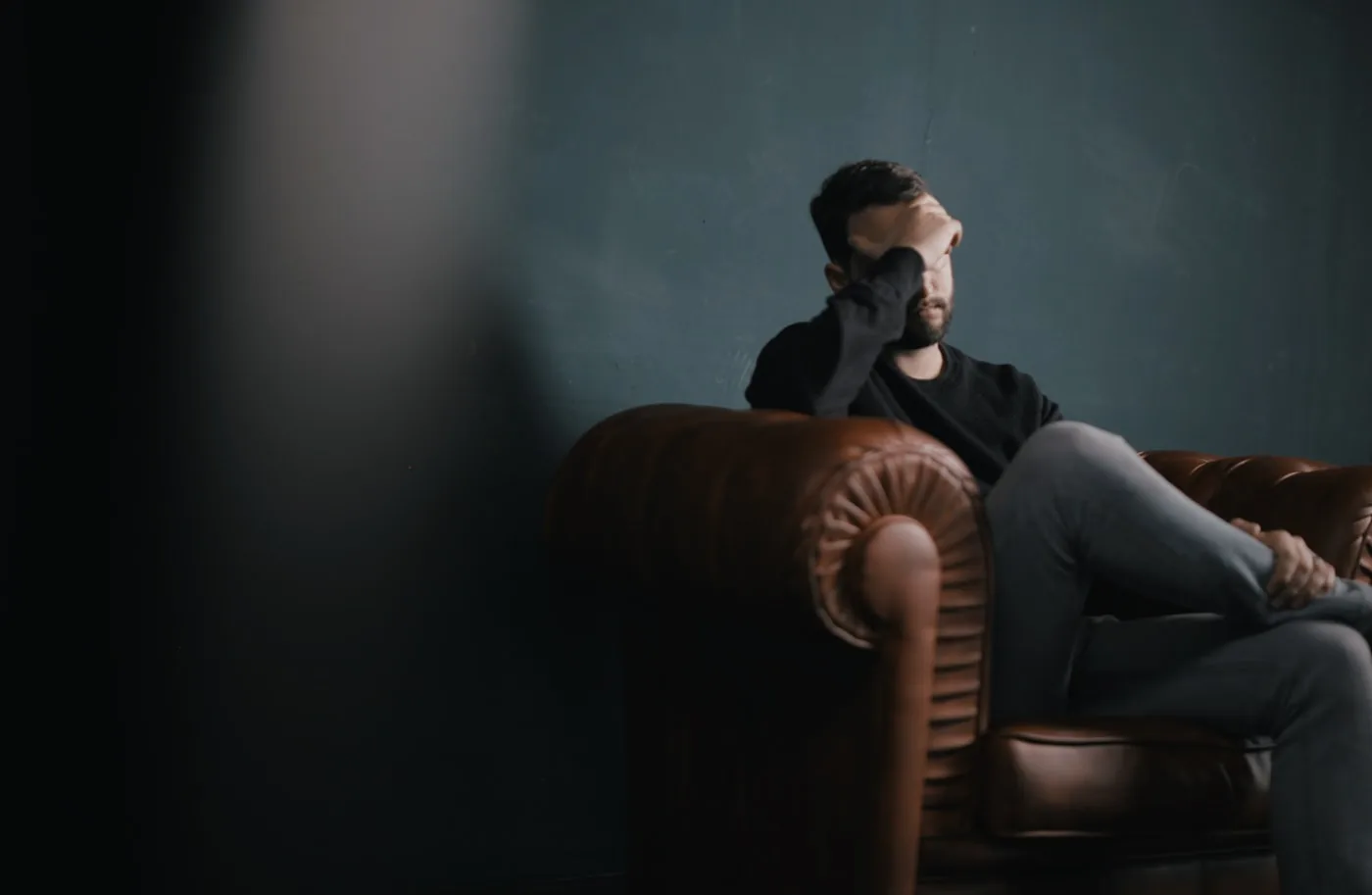 Personne assise sur un canapé, main sur le front, évoquant la fatigue et la douleur chronique.